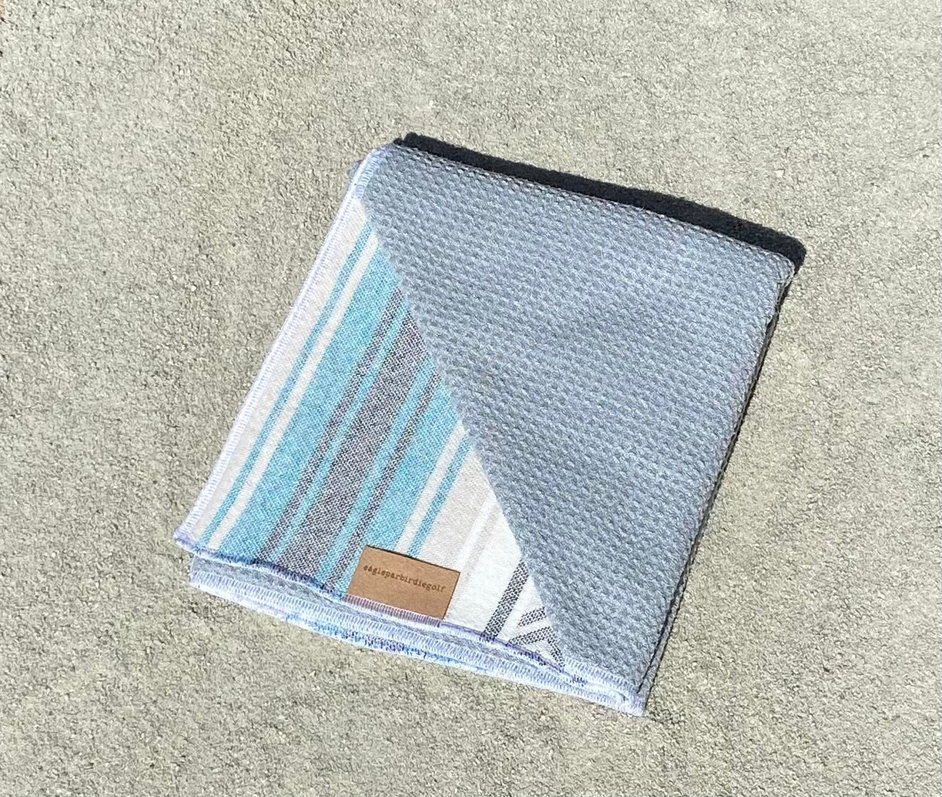 Folded Teal Baja Surf Golf Towel with Gray Interior on Sand