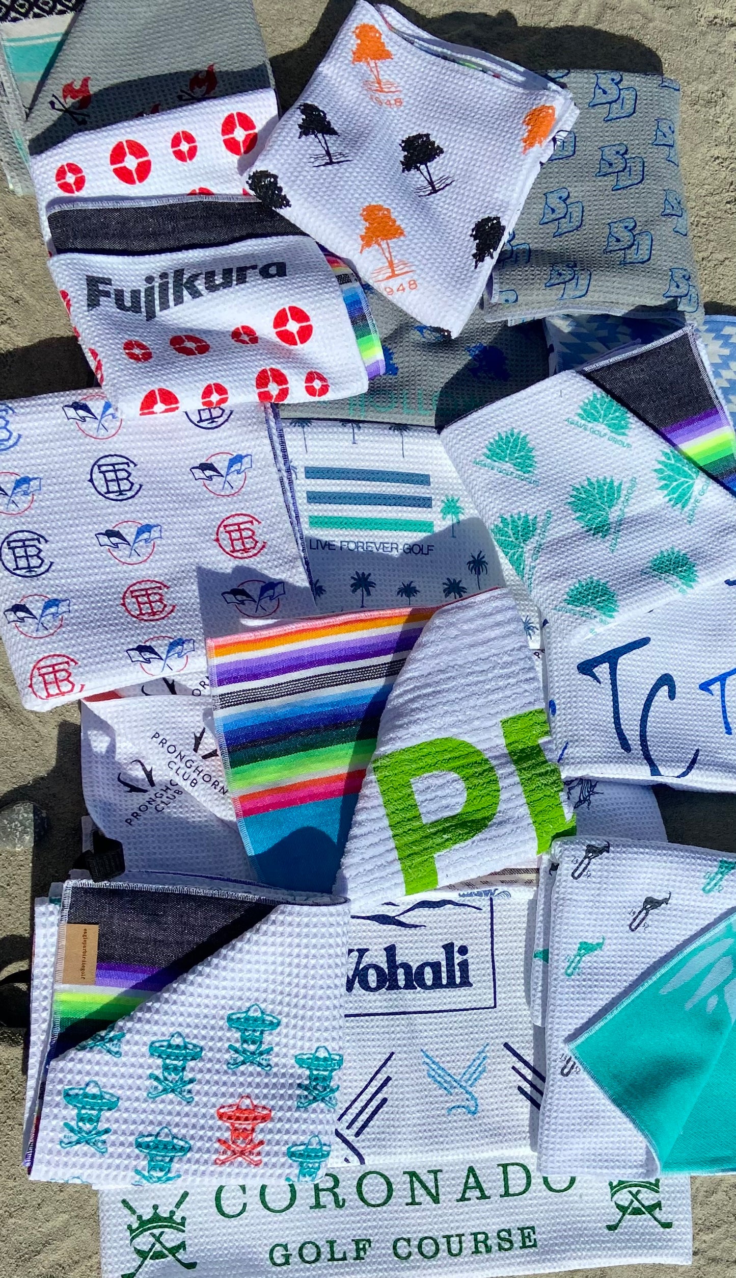 Pile of Colorful Golf Towels with Custom Logos on Sand
